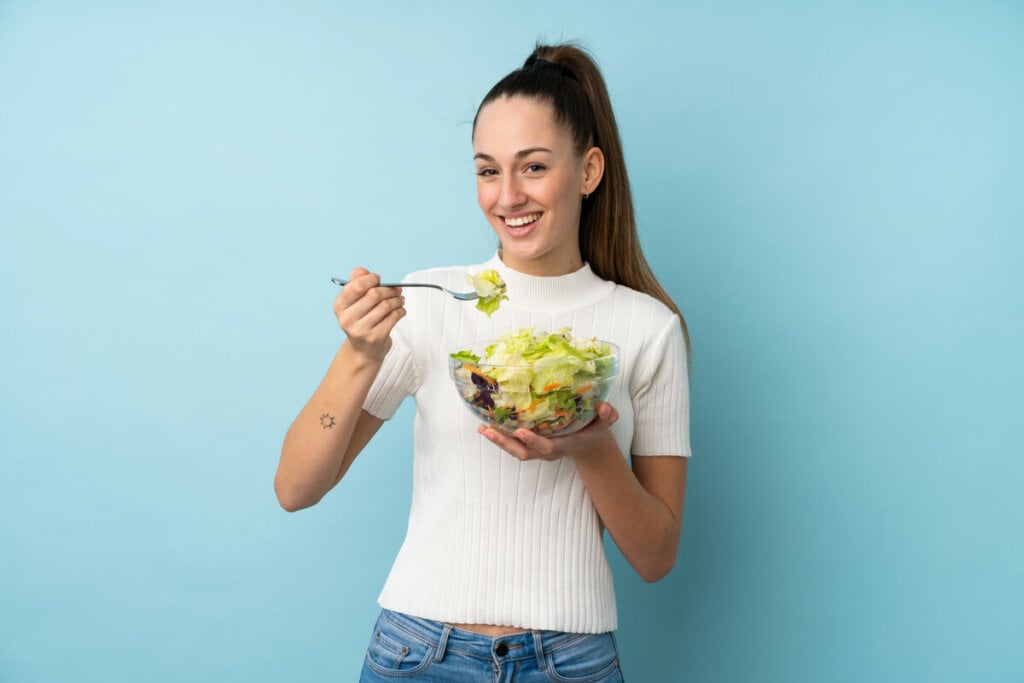 Mulher comendo salada em fundo azul