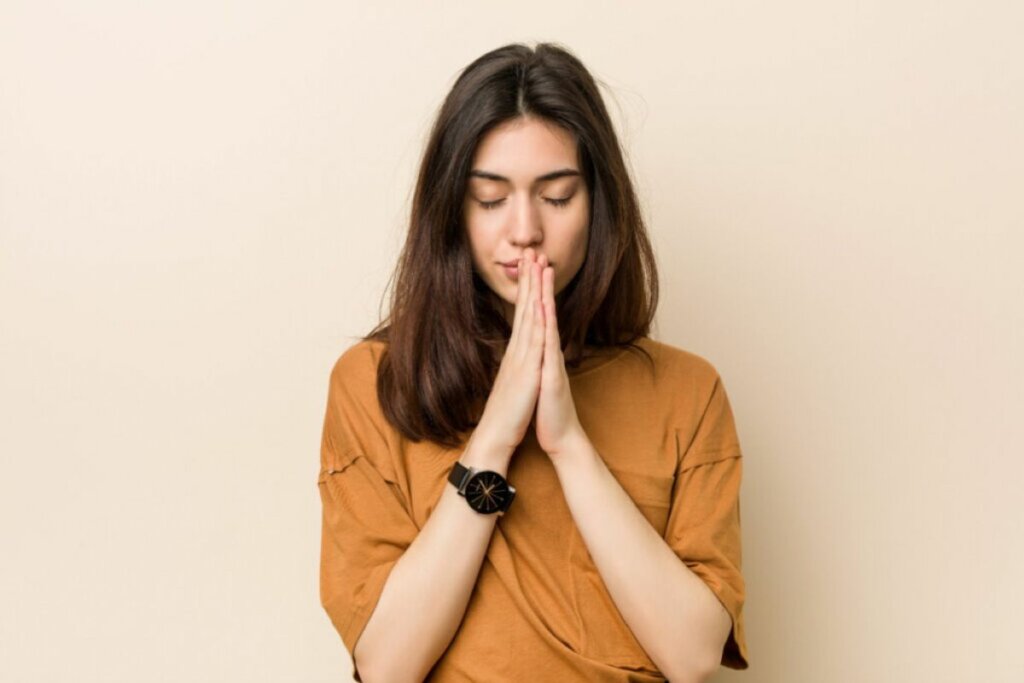 Mulher com camiseta marrom e olhos fechados rezando