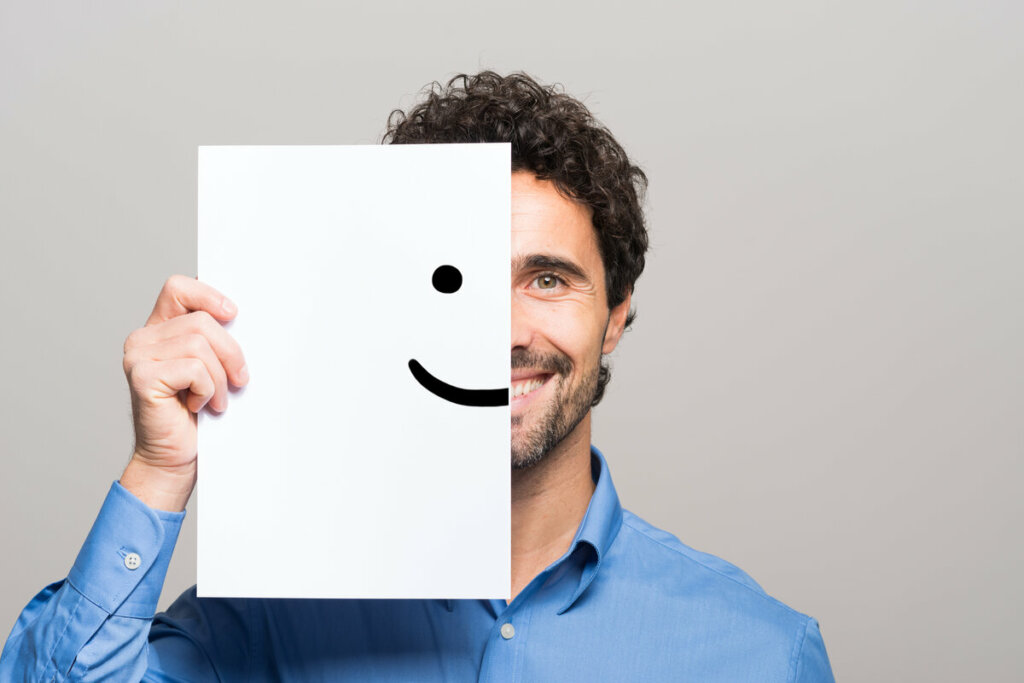 Homem sorrindo segurando um papel com o desenho de um sorrindo no rosto 