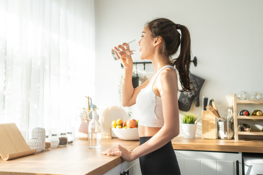 Mulher com roupas esportivas bebendo água após exercício em casa