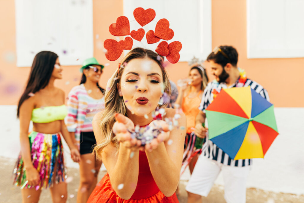 Mulher com roupa de Carnaval assoprando confete nas mãos