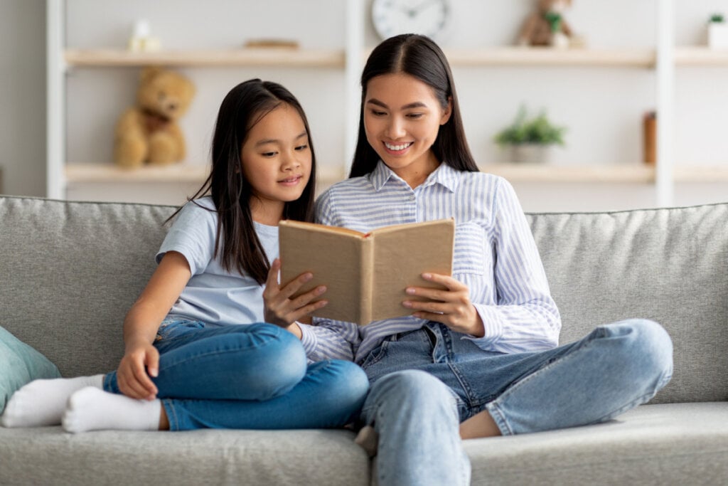 Mãe e filha lendo livro juntas no sofá