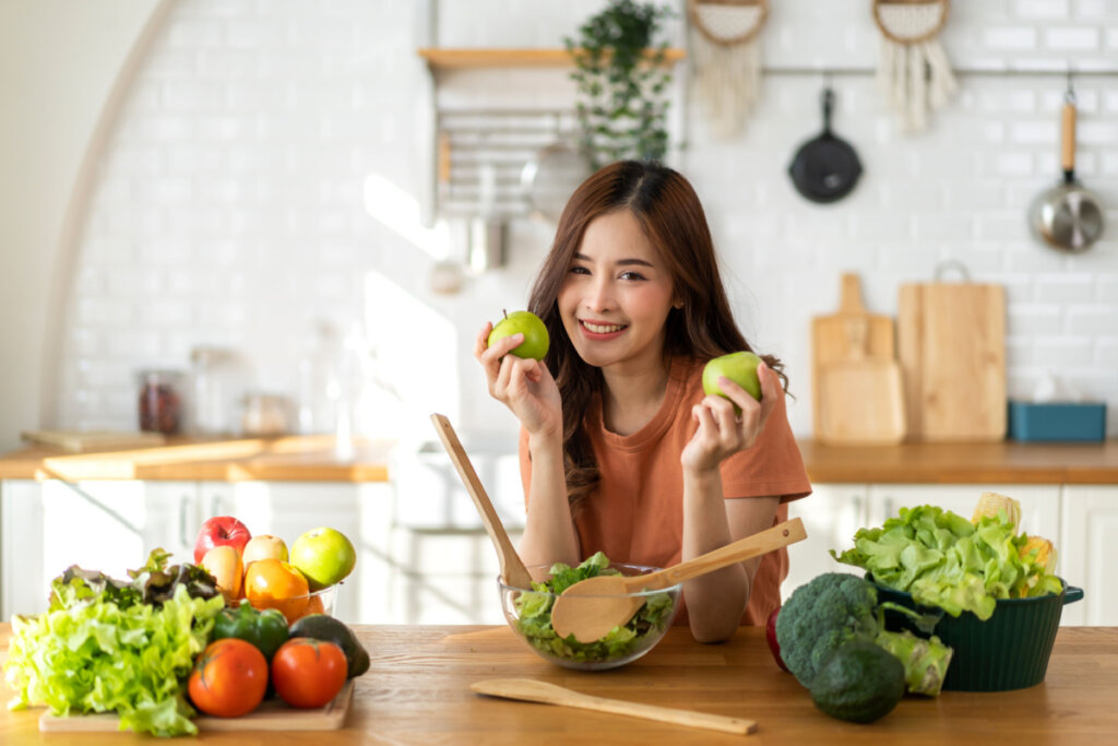 Menina segurando maçãs e com diversos vegetais a sua frente