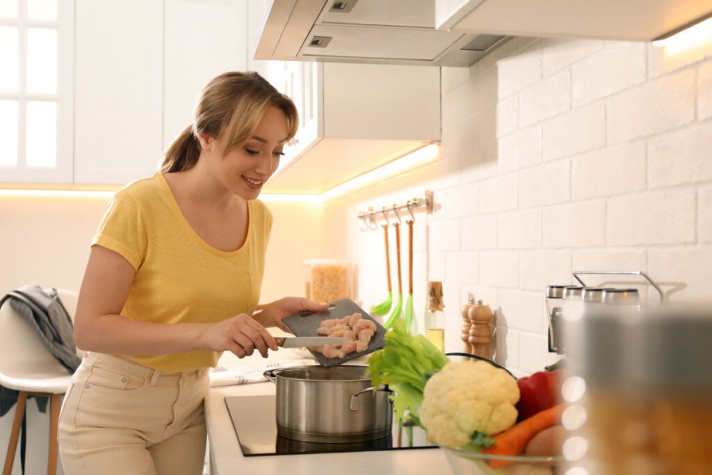 Mulher na cozinha colocando pedaços de frango em panela