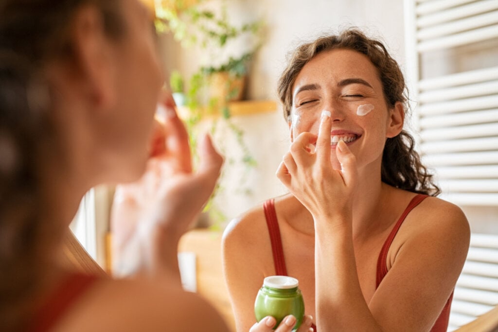 Mulher em frente ao espelho aplicando creme no rosto