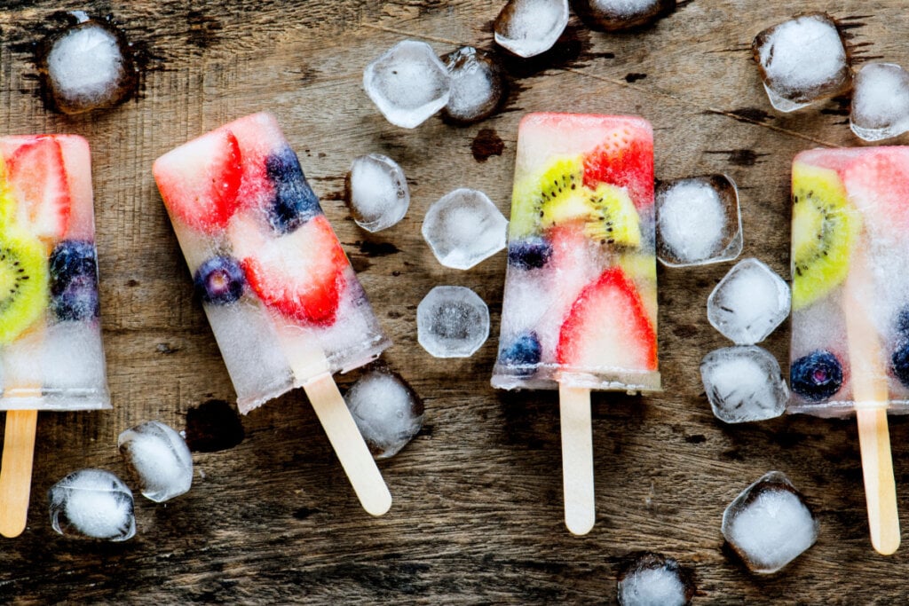 4 picolés de frutas com água de coco e pedras de gelo em volta