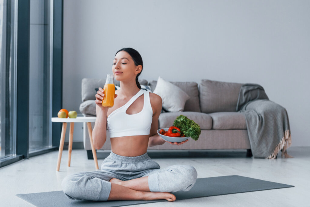 Mulher segurando alimentos saudáveis e sentada em tapete de yoga