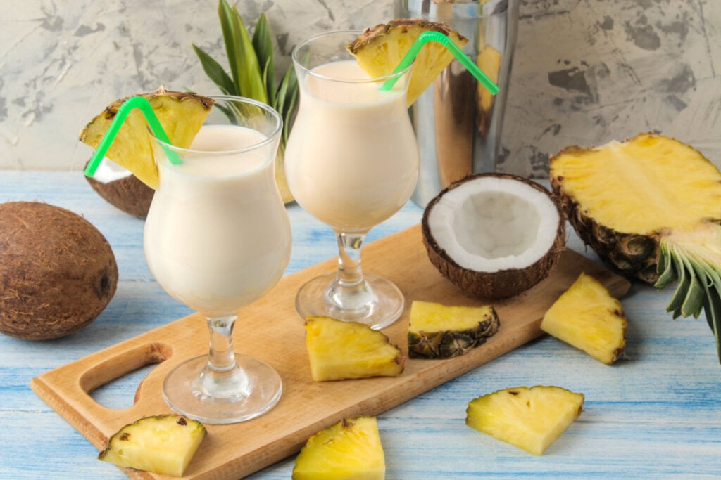 Vitamina de coco e abacaxi em taças e coco e abacaxi cortados ao redor