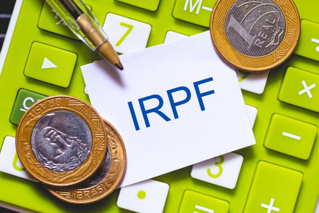 Papel escrito "IRPF" em cima de uma calculadora verde com moedas e caneta 