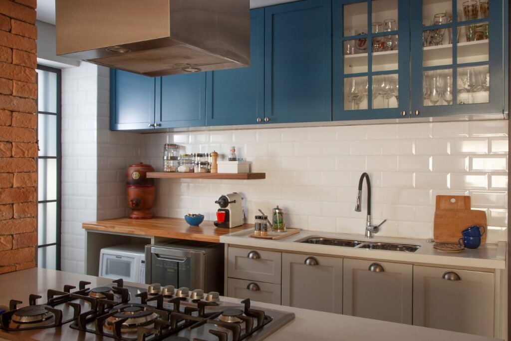 Cozinha com móveis azul e azulejo branco com porta lateral