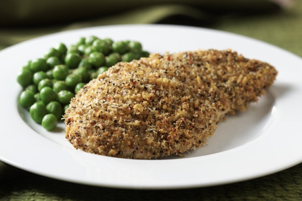 Frango com crosta de castanha em cima de um prato branco com ervilhas