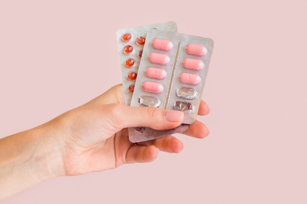 Mãos feminina segurando duas cartelas de remédio em um fundo rosa