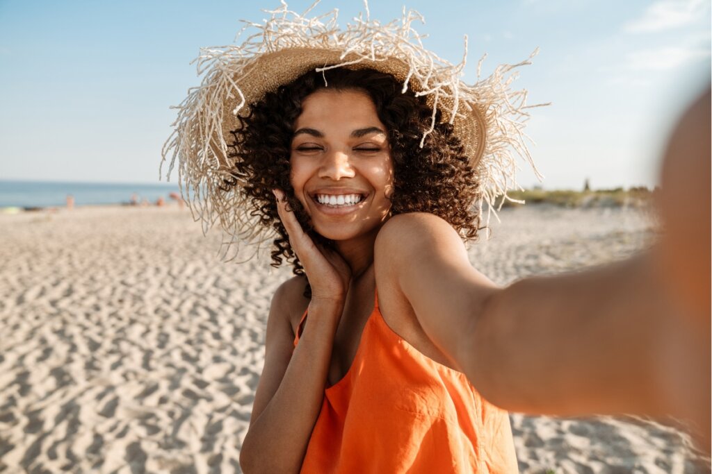 Mulher usando blusa laranja e chapéu tomando na praia