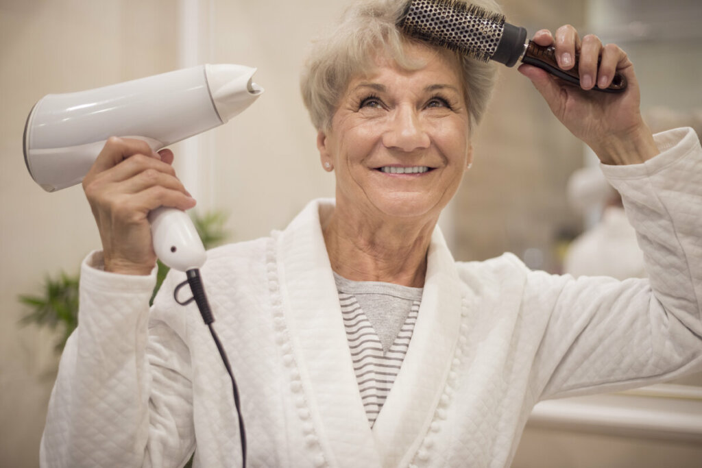 Mulher de meia-idade secando o cabelo em frente a um espelho 