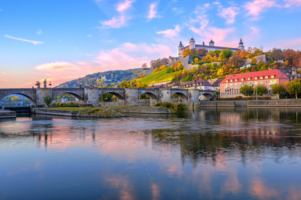 Paisagem com rio e castelo ao fundo com o céu azul e rosa