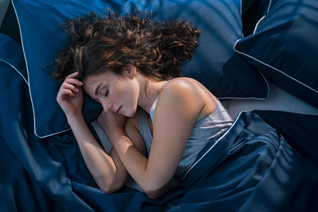 Foto de uma mulher dormindo em uma cama com fronhas e lençóis azuis.