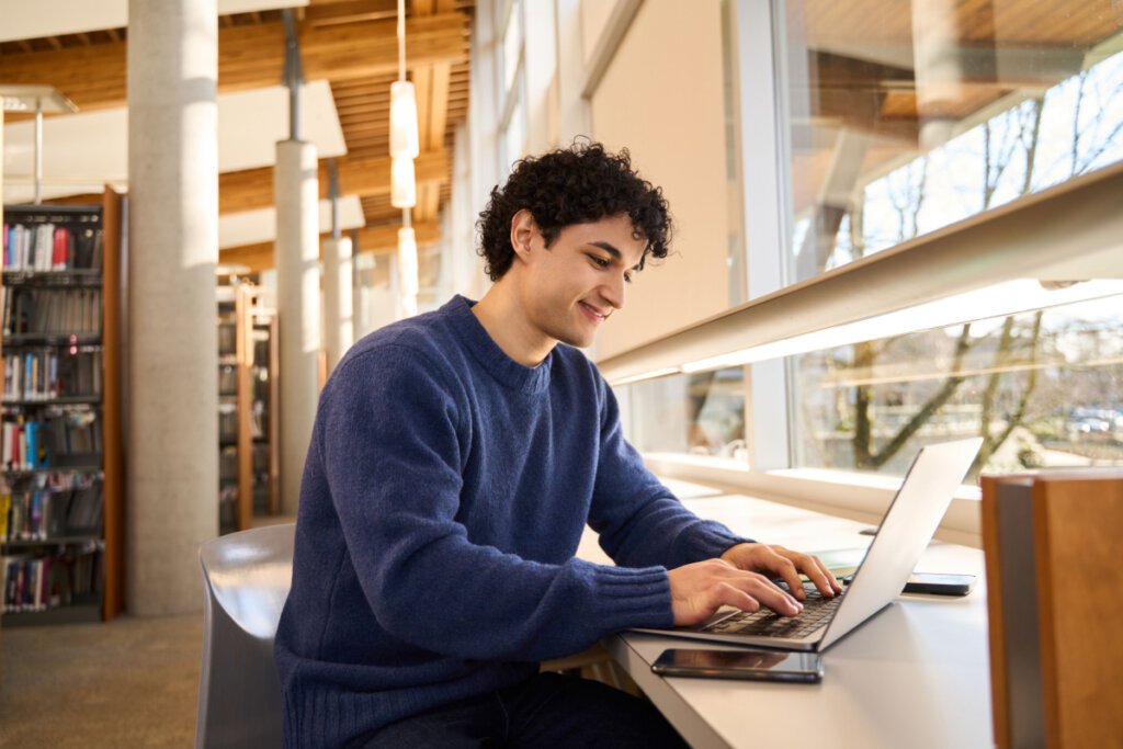 Estudante em uma biblioteca sorrindo enquanto usa o notebook