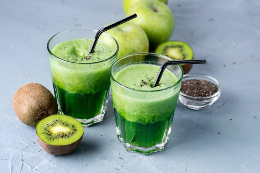 Copo de vidro com suco verde e kiwi e maçã-verde ao redor