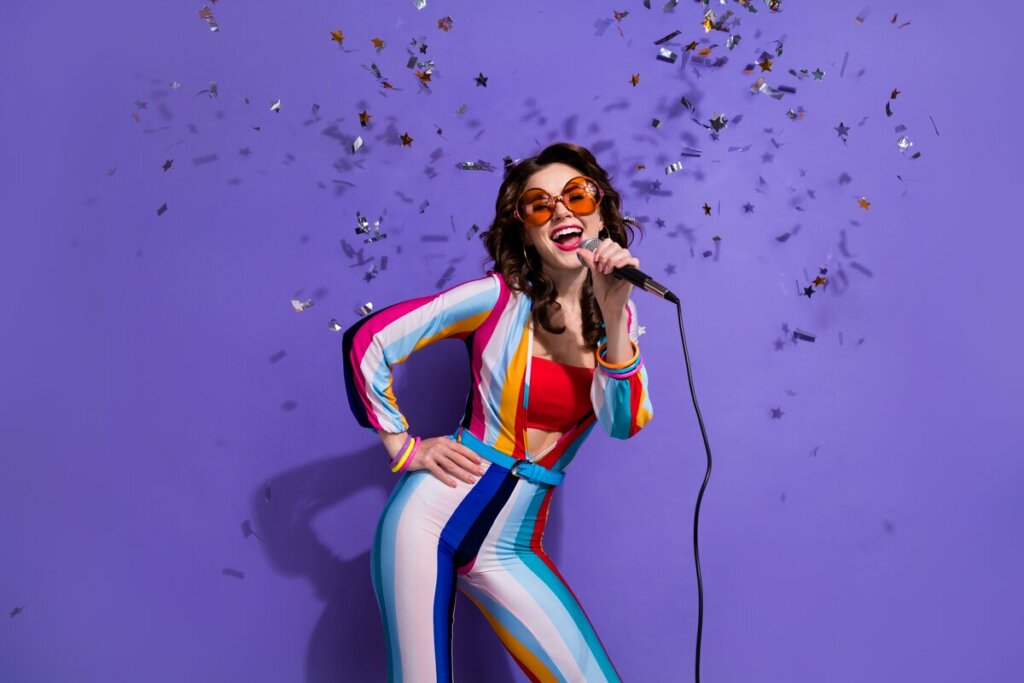 Mulher vestida com macacão colorido cantando em um microfone