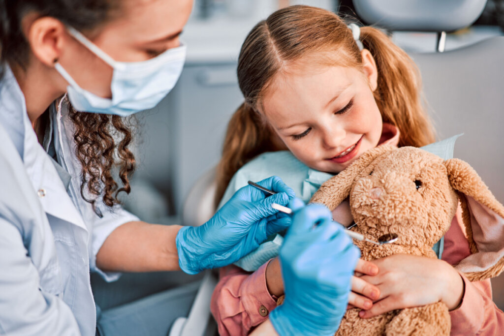 Dentista examinando ursinho em colo de menina pequena