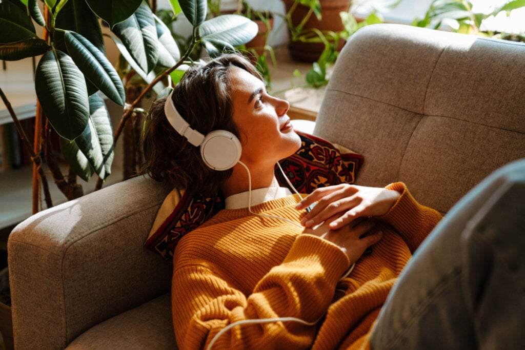 jovem deitada em sofá ouvindo musica no fone de ouvido