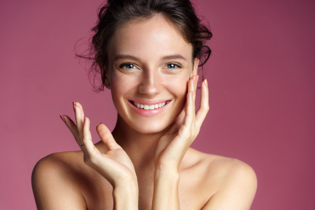 Mulher com a mão no rosto aplicando maquiagem em um fundo rosa 
