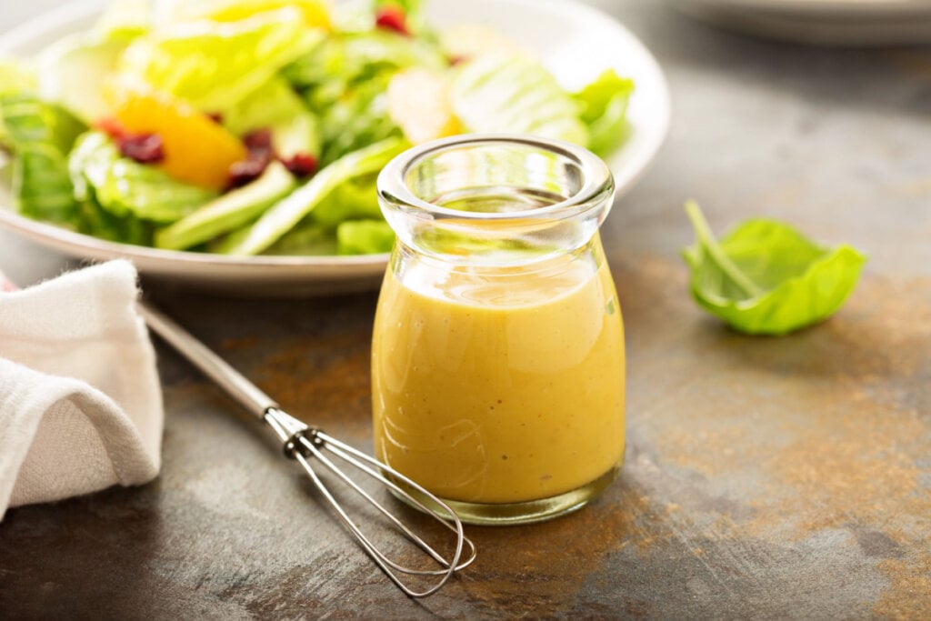 Molho amarelo em pote de vidro com salada ao fundo