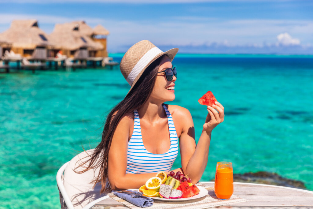 Mulher comendo frutas em mesa na praia
