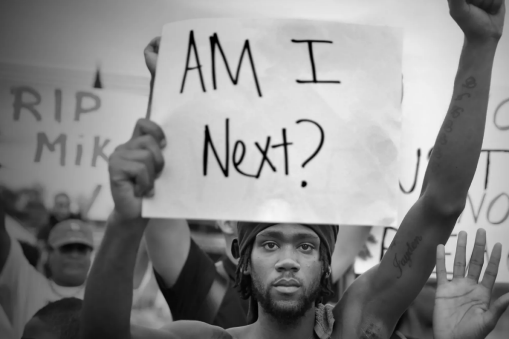 Homem negro com uma placa na mão onde está escrito "Eu sou o próximo?"