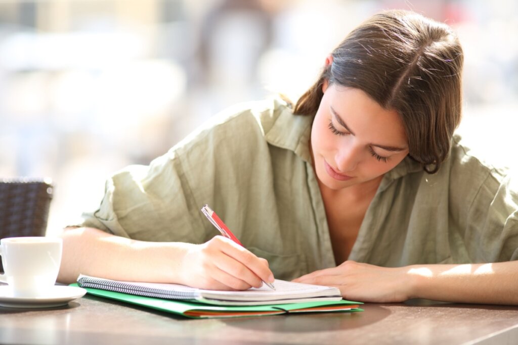 Estudante escrevendo em um caderno com uma xícara ao lado