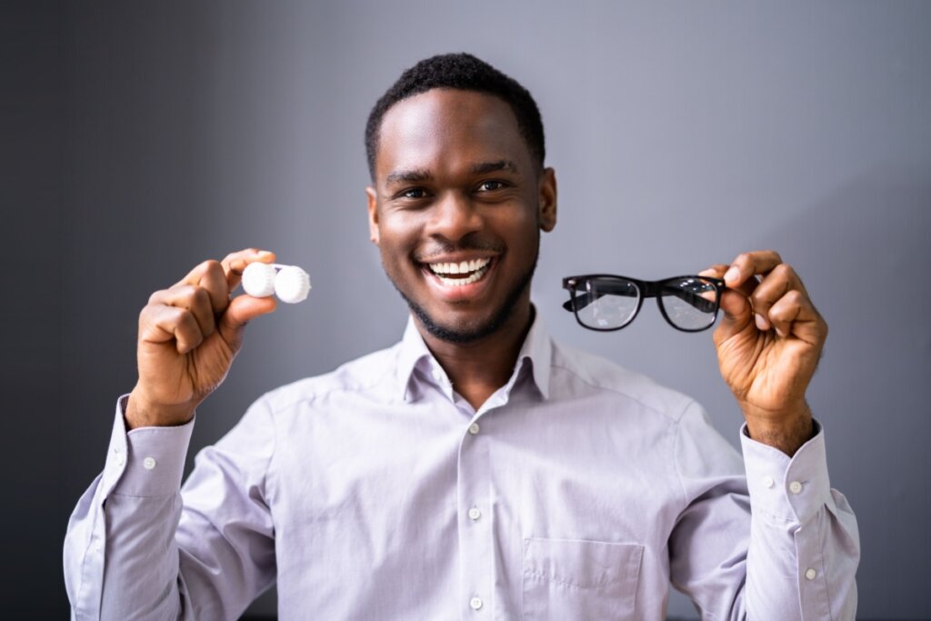 Homem segurando óculos em uma mão e caixa da lente de contato em outra mão