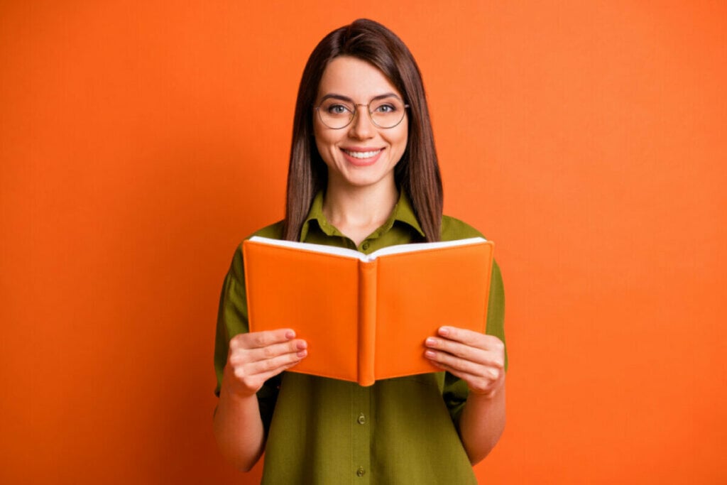 Mulher com blusa verde usando óculos e segurando um livro