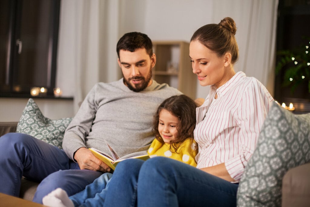 Homem e mulher sentados em um sofá com uma menina segurando um livro