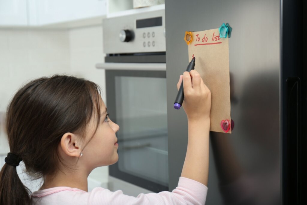 Criança escrevendo em papel preso em geladeira