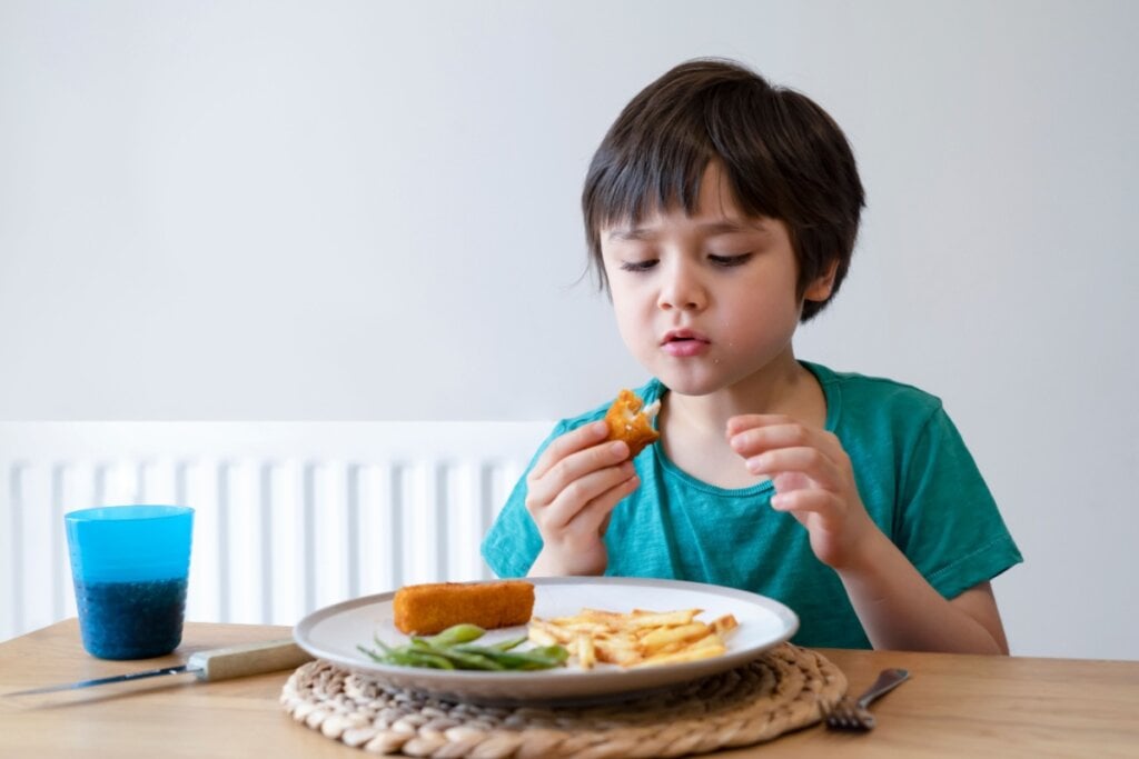 Menino comendo peixe e batata frita