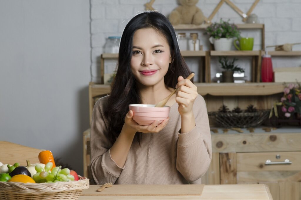 Mulher asiática segurando um bowl e uma colher olhando para a câmera