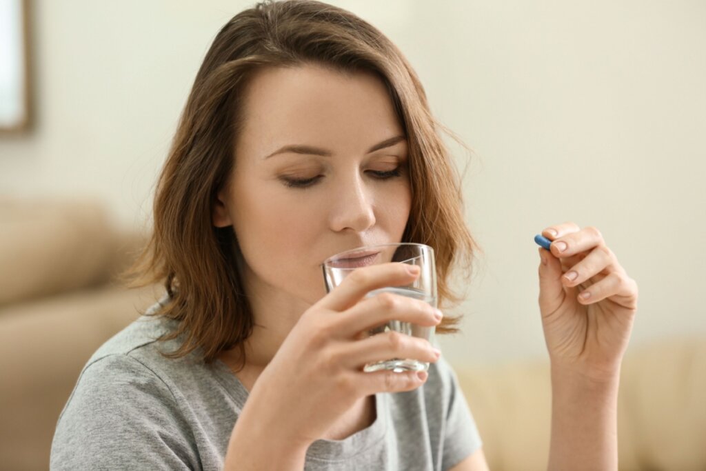Mulher jovem segurando um comprimido em uma mão enquanto vai beber água.