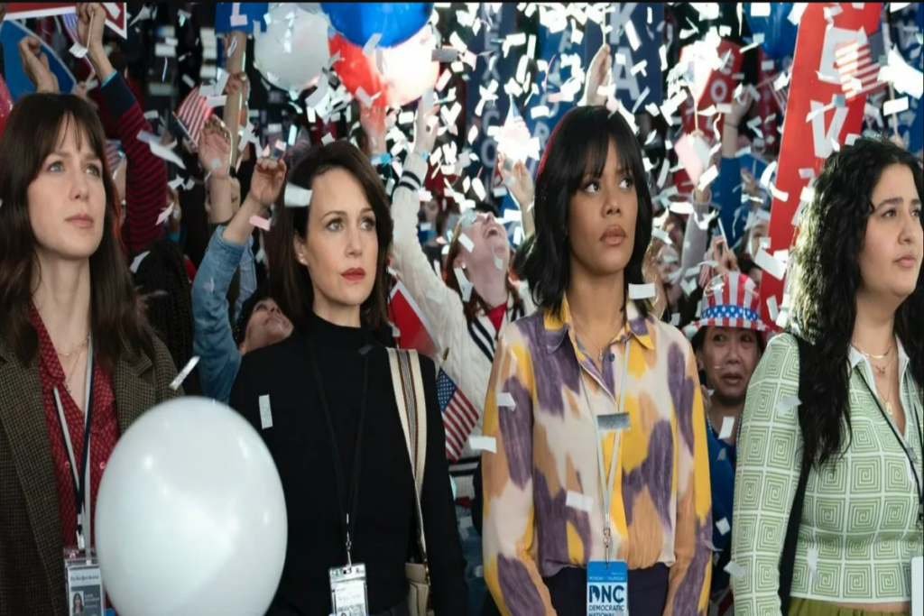 Quatro mulheres com expressões sérias, ao fundo uma comemoração com balões e confetes