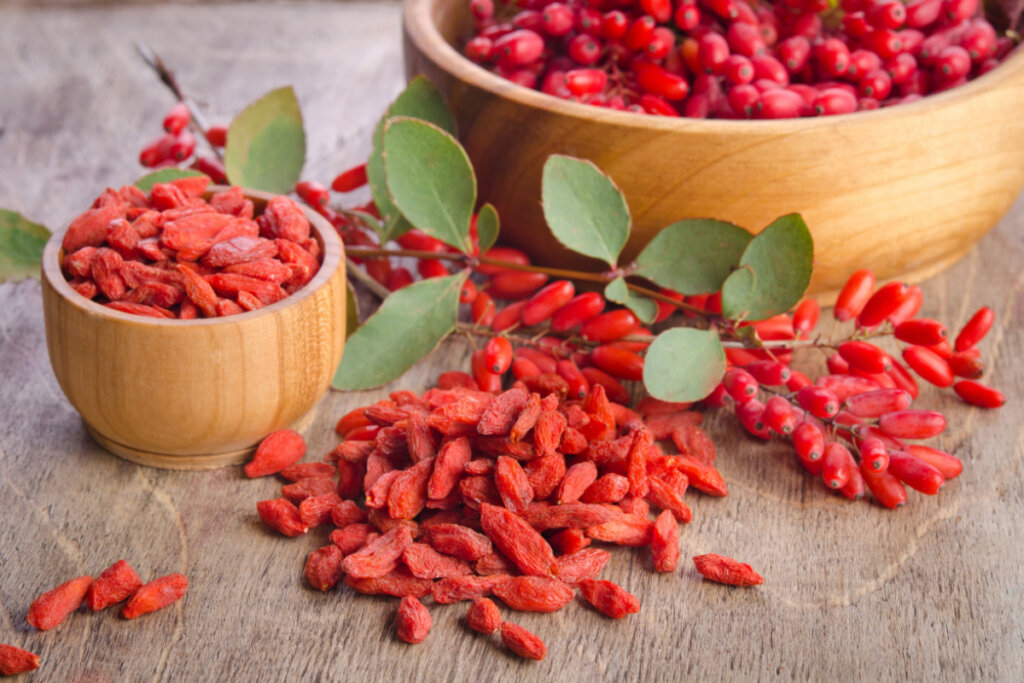 Fruta goji berry dentro de cumbucas de madeira e espalhada ao redor em uma bancada