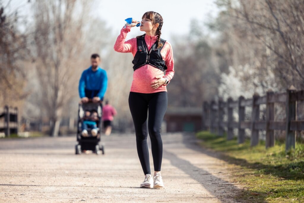 Mulher grávida caminhando e bebendo água em parque