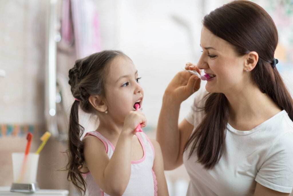 Mãe e filha pequena no banheiro escovando os dentes