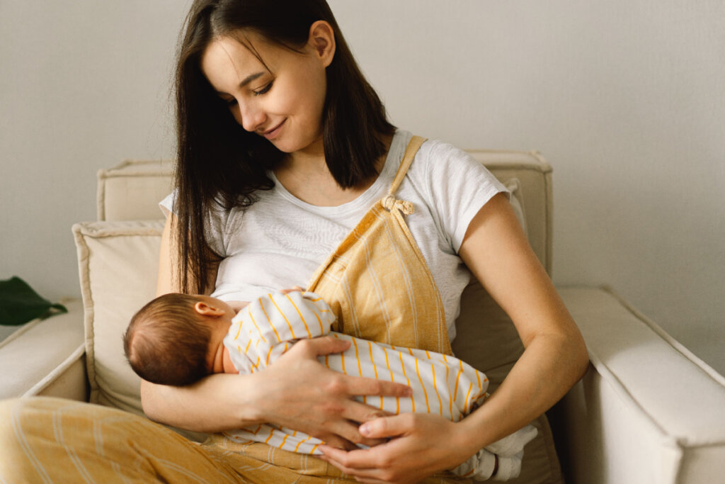 Mãe sentada em poltrona e bebê sendo aninhado por ela em seus braços