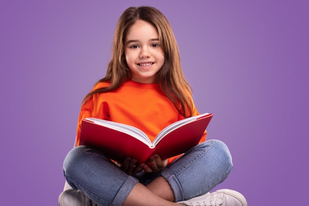 Menina sentada no chão lendo livro com capa vermelha