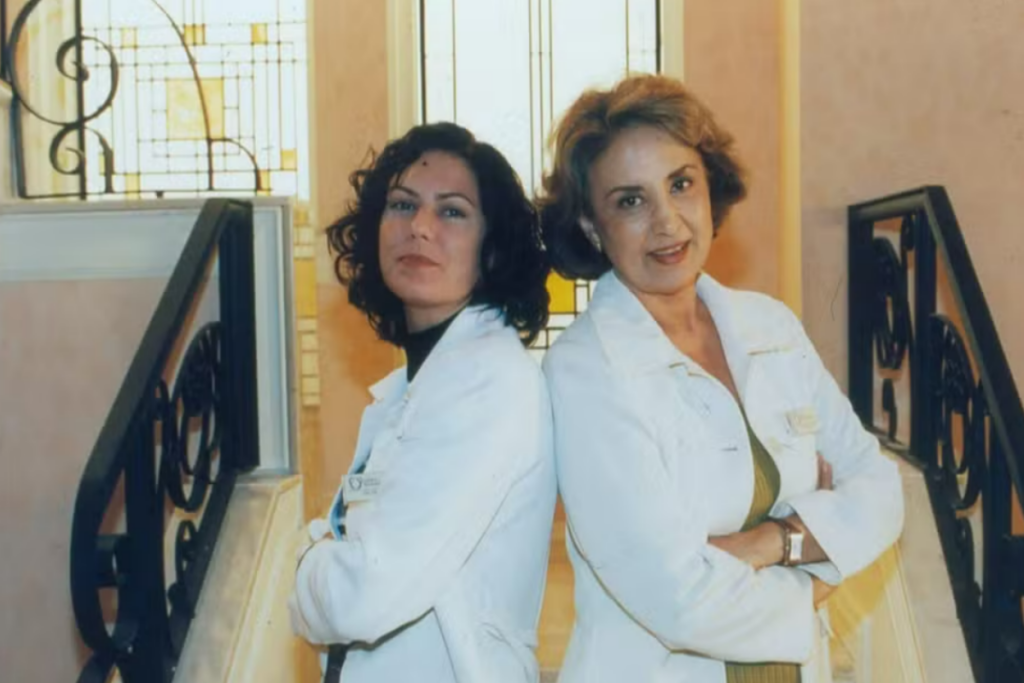 duas mulheres de cabelo curto e jaleco de médica em frente a uma escada