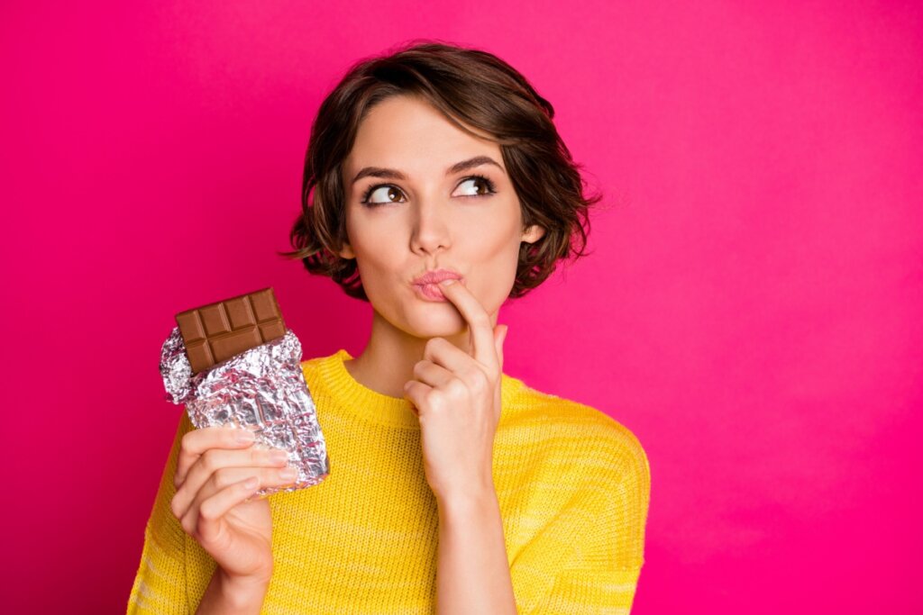 Mulher segurando chocolate e com dedo na boca