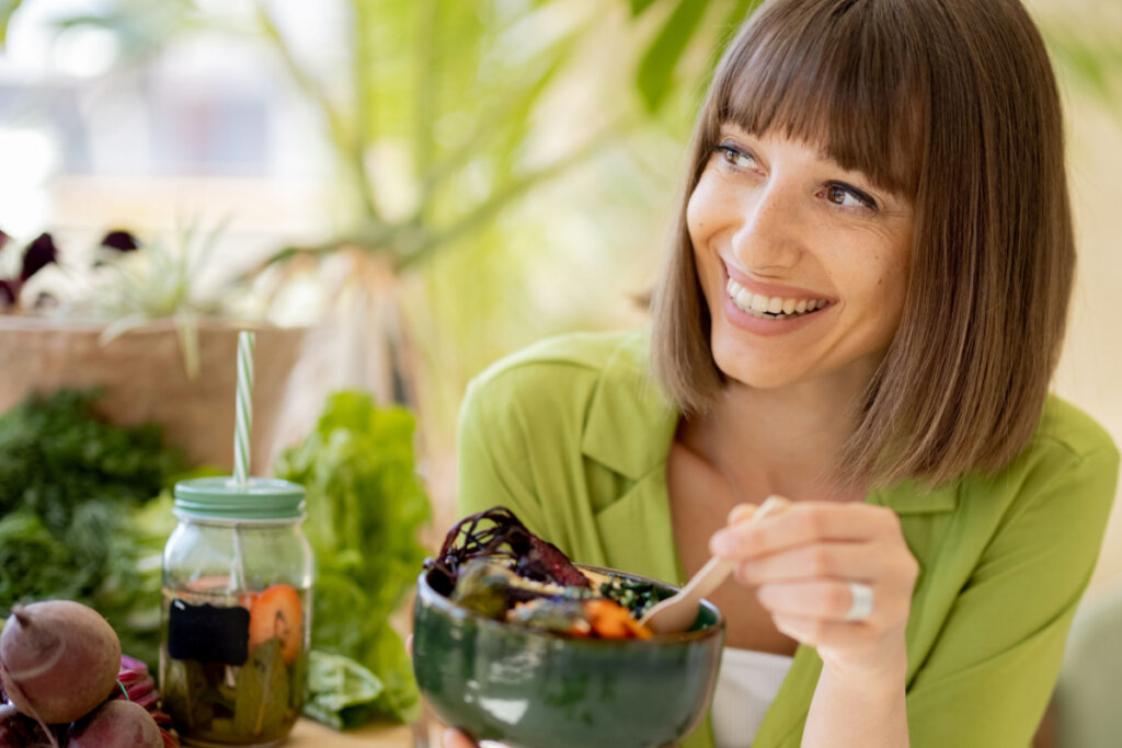 Mulher de camiseta verde, sorrindo e segurando pote com comida saudável