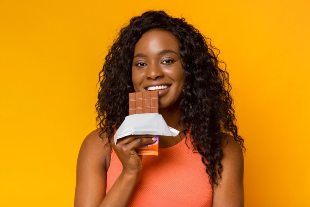 Mulher com uma barra de chocolate na mão em um fundo laranja