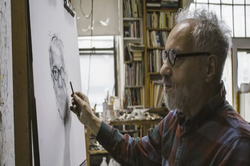 Homem grisalho de camisa xadrez e óculos pintando um autorretrato