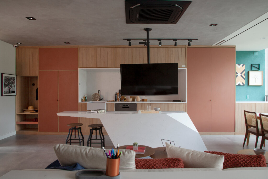 Espaço de estar e cozinha integrados com decoração moderna: armários de madeira, uma ilha de cozinha branca e área de estar com televisão plana, realçados por uma paleta de cores terrosas 