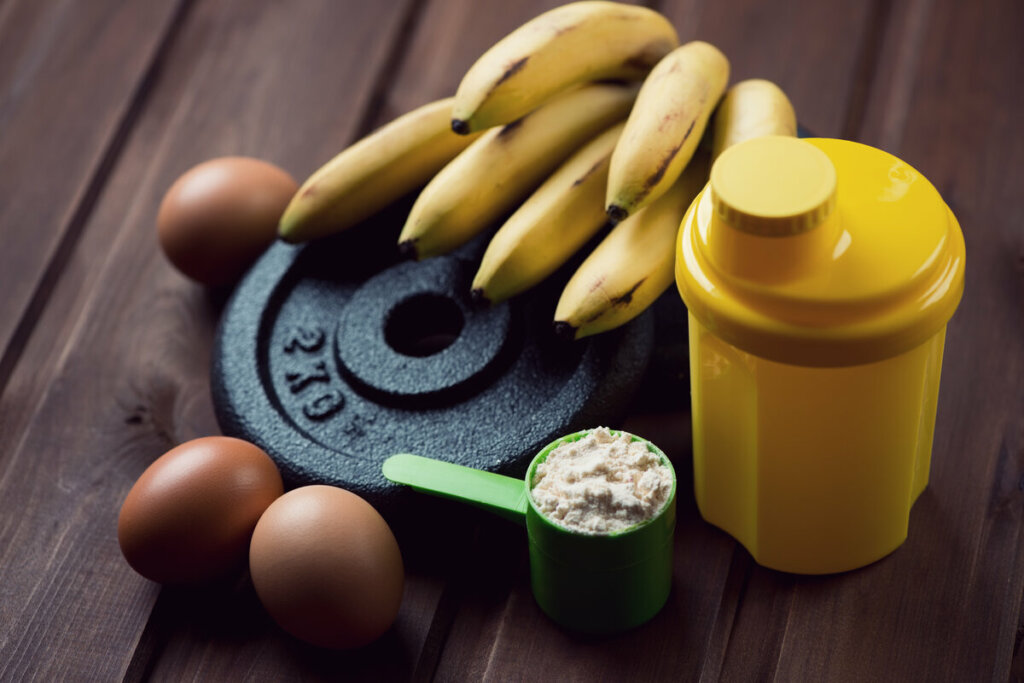 Peso de musculação com bananas, ovos e uma garrafa em cima de uma mesa de madeira